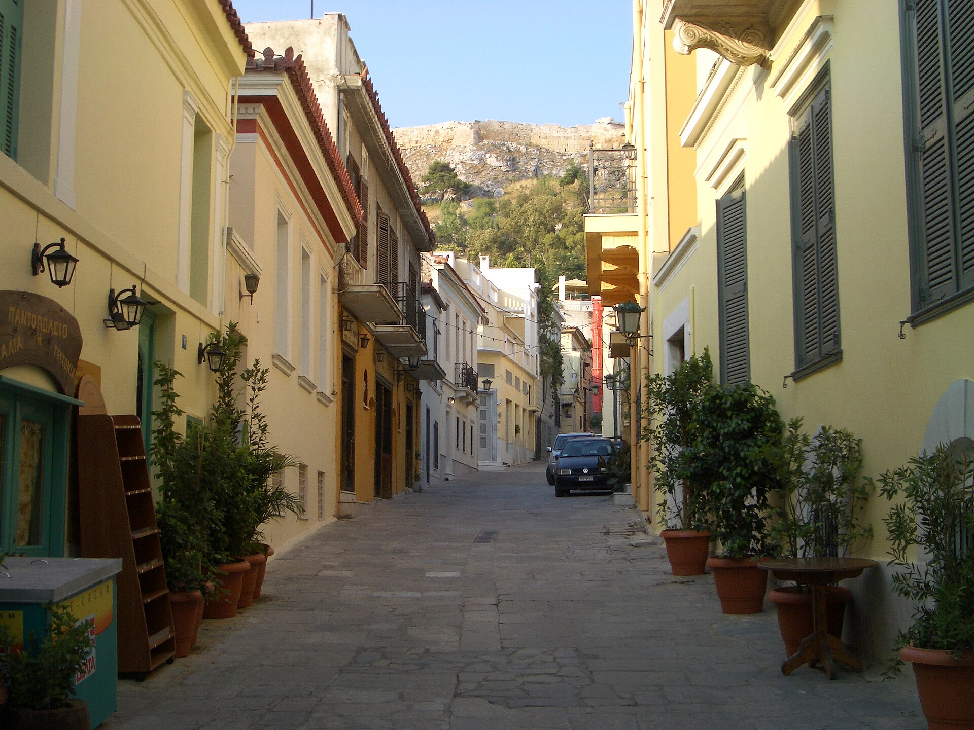 A pedestrian street in Plaka, Athens, lined with low buildings and cafe tables.